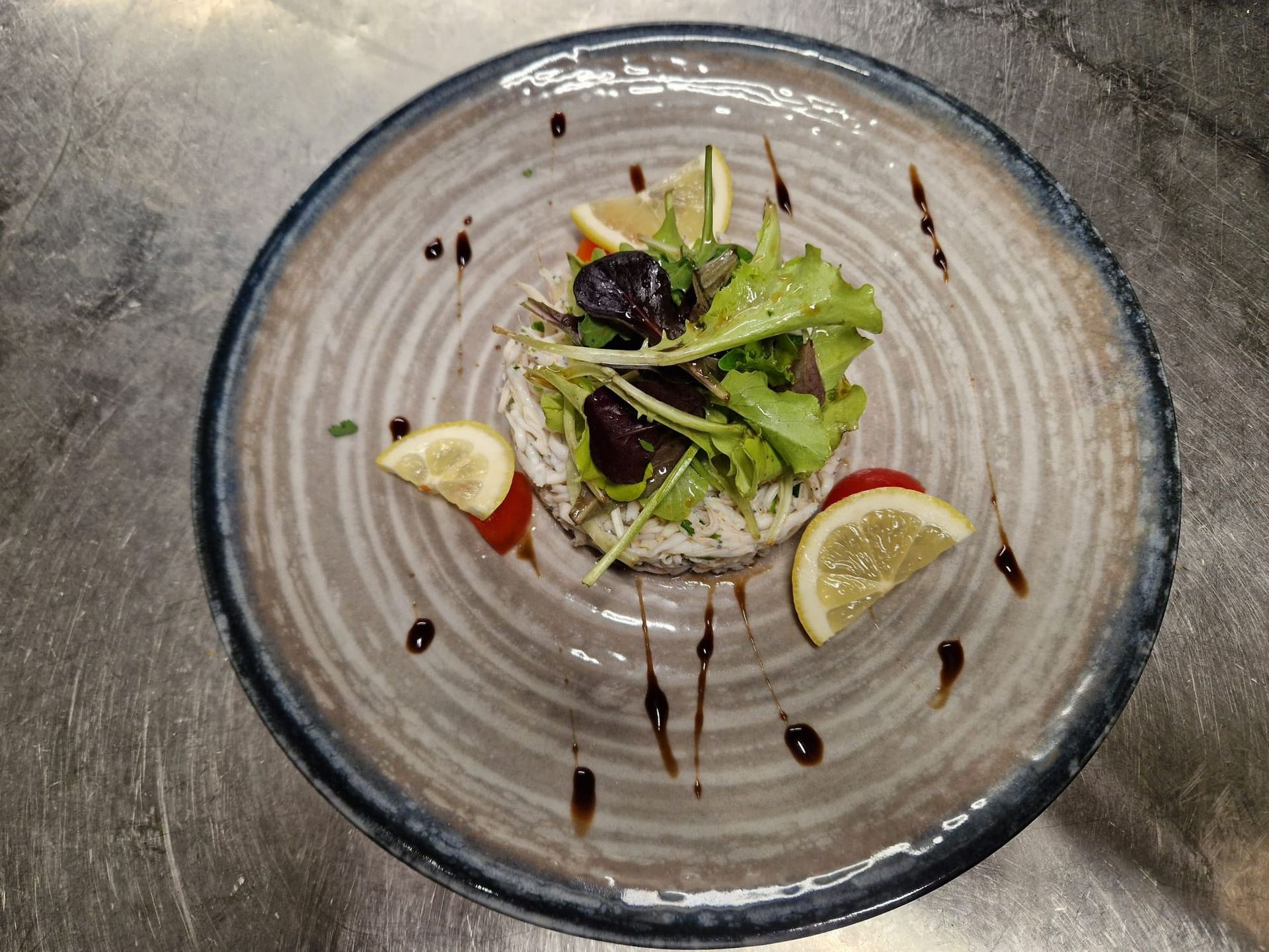 Antipasto di insalata di granchio su un piatto rustico, guarnito con verdure, fette di limone e glassa balsamica.