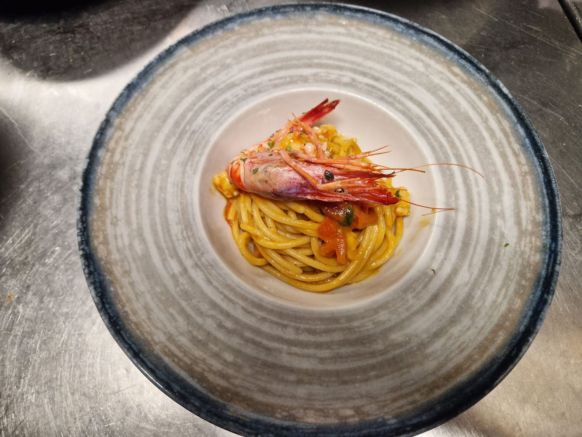 Piatto di pasta: spaghetti al sugo, conditi con gamberi alla griglia, serviti in una ciotola di ceramica.