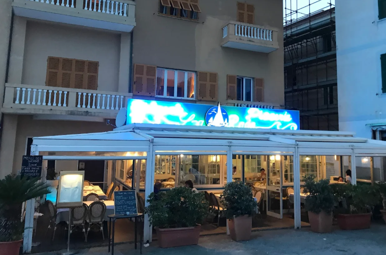 Esterno del ristorante al tramonto con insegna illuminata in blu e posti a sedere all'aperto.