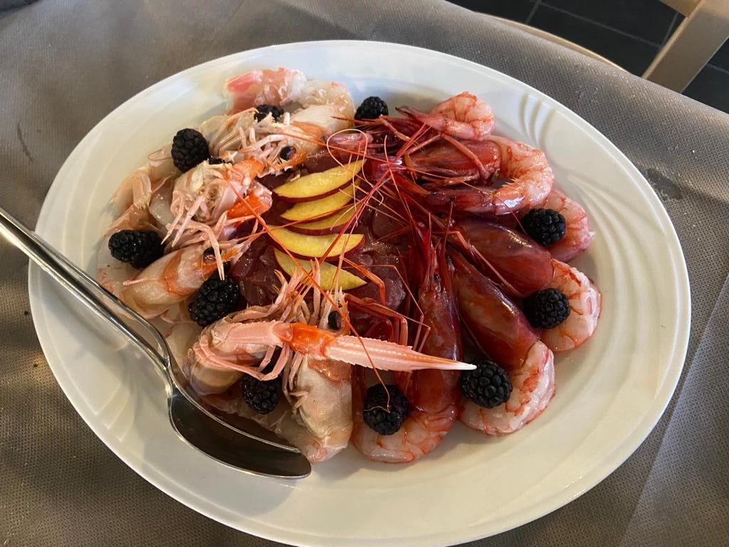 Piatto di gamberi cotti con more e fette di pesca.