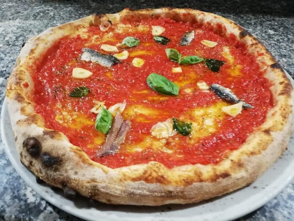 Pizza con salsa di pomodoro, aglio, acciughe e basilico su un piatto bianco.