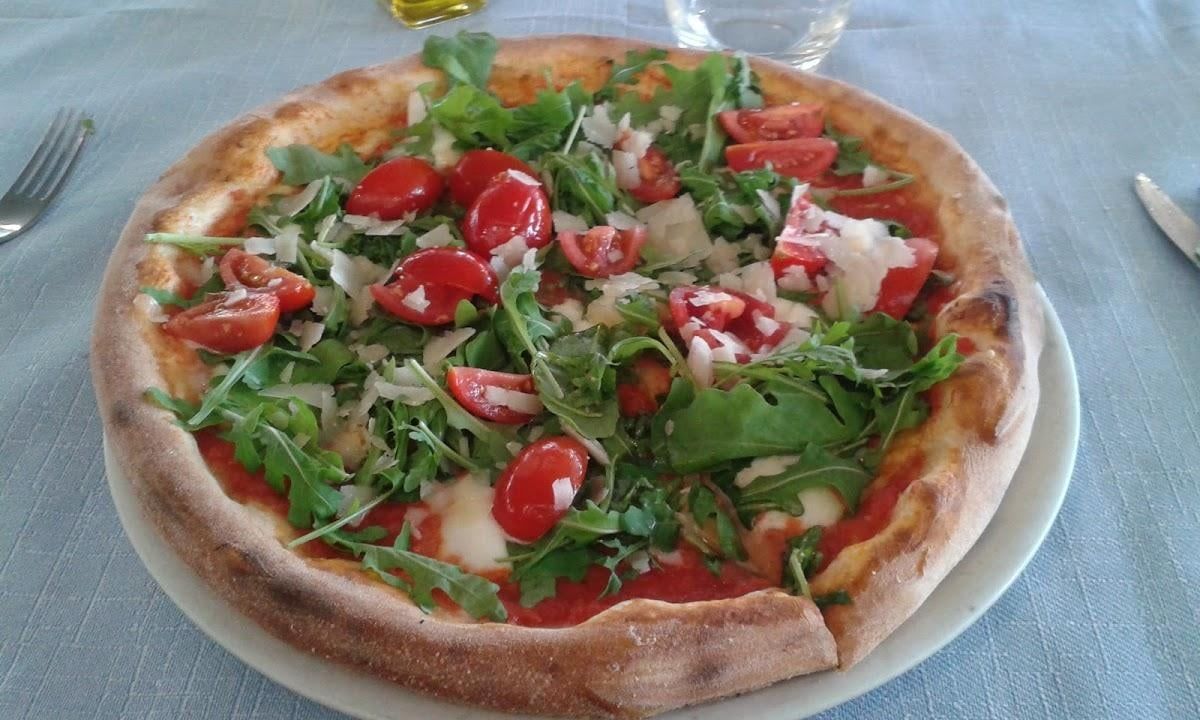 Pizza con rucola, pomodori e parmigiano su un piatto bianco.