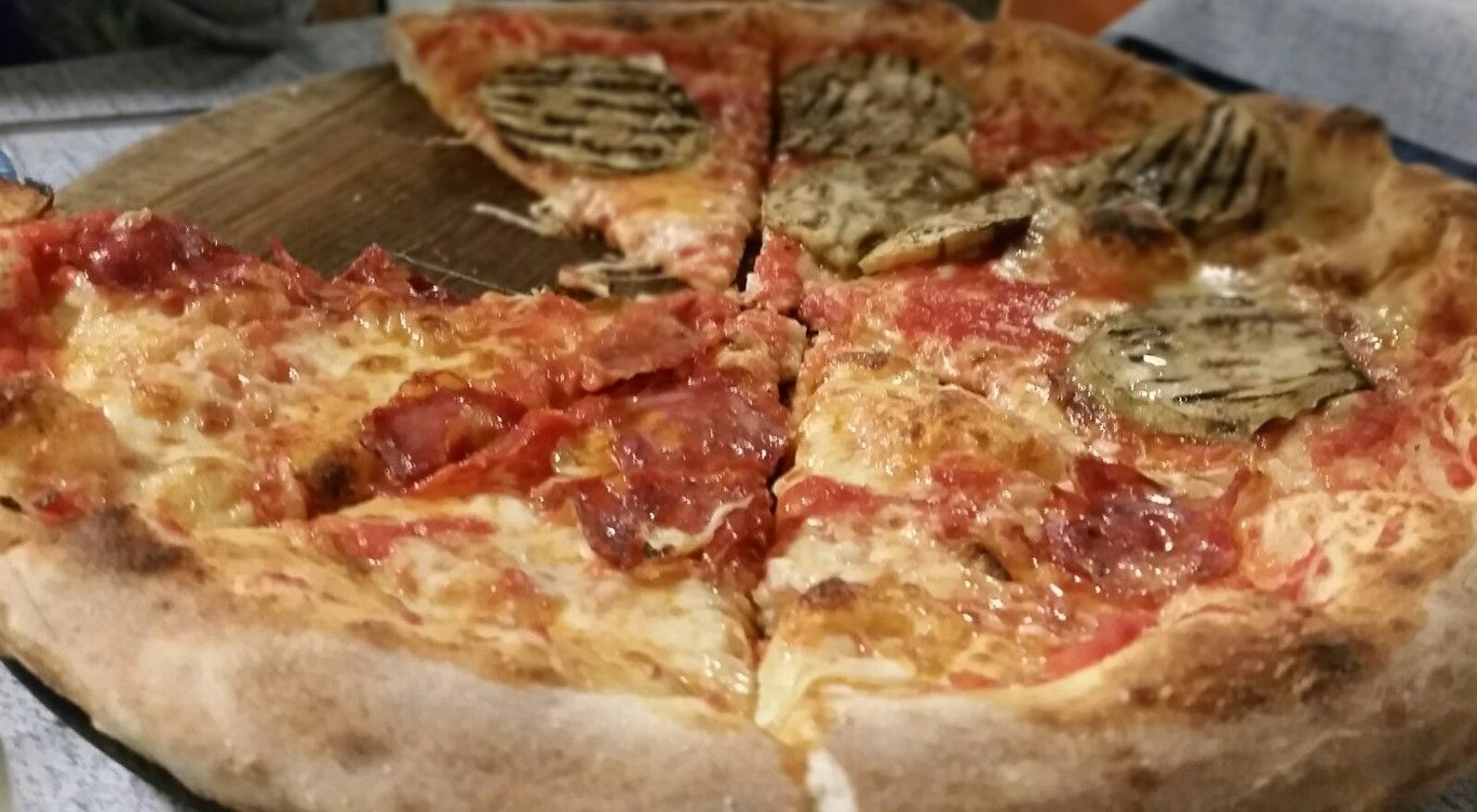 Pizza con peperoni e verdure affettate su una superficie di legno.