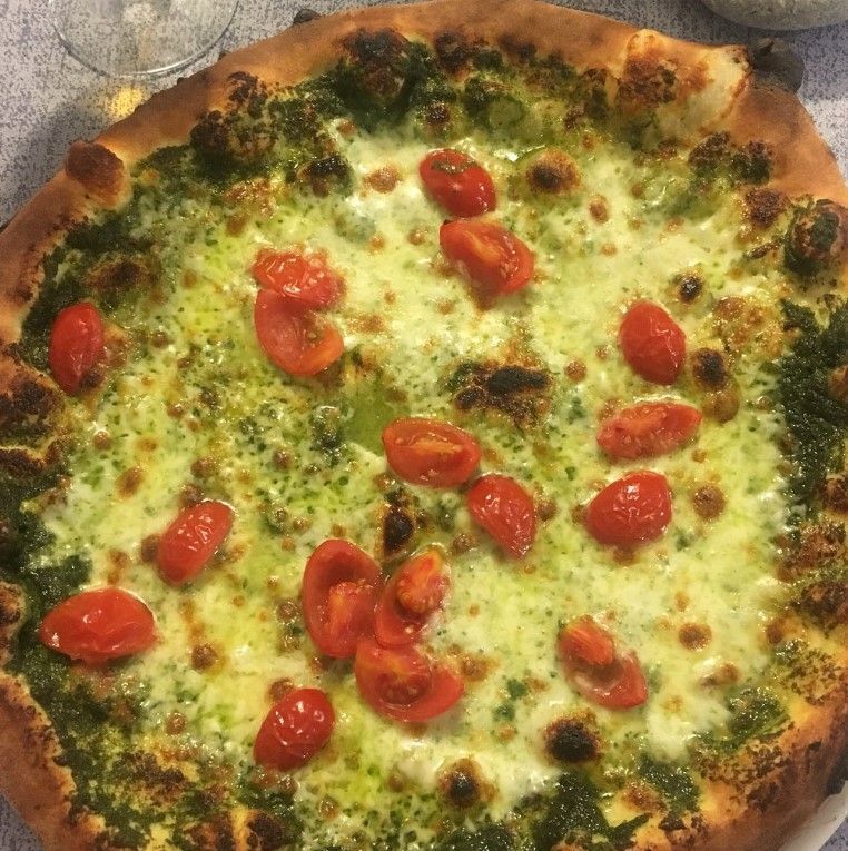 Pizza con pesto verde, mozzarella e pomodorini rossi.