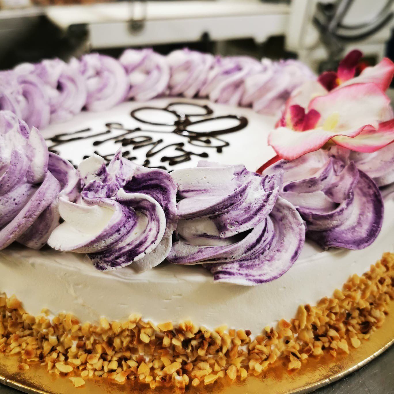 Torta con glassa viola e bianca a spirale, decorata con un fiore commestibile e noci intorno alla base.