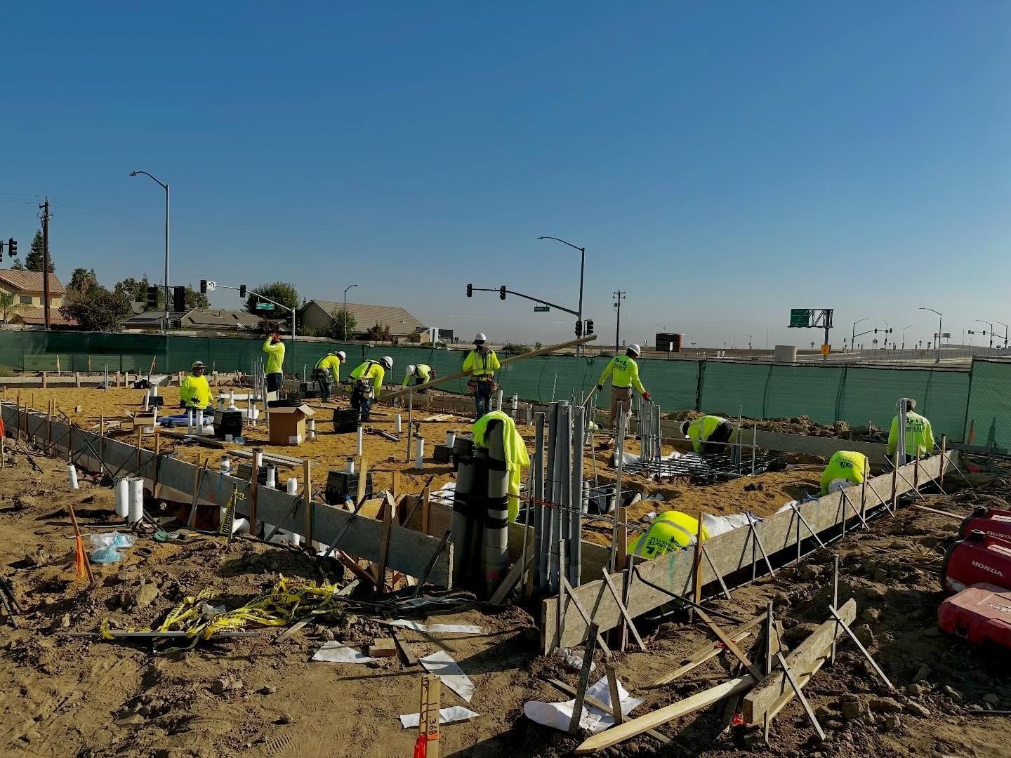 Construction workers pouring concrete at a road intersection under a clear blue sky
