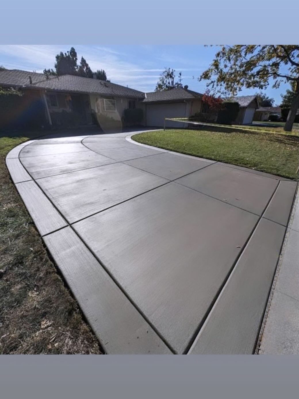 Curved concrete driveway leading to a suburban house with a green lawn on a sunny day