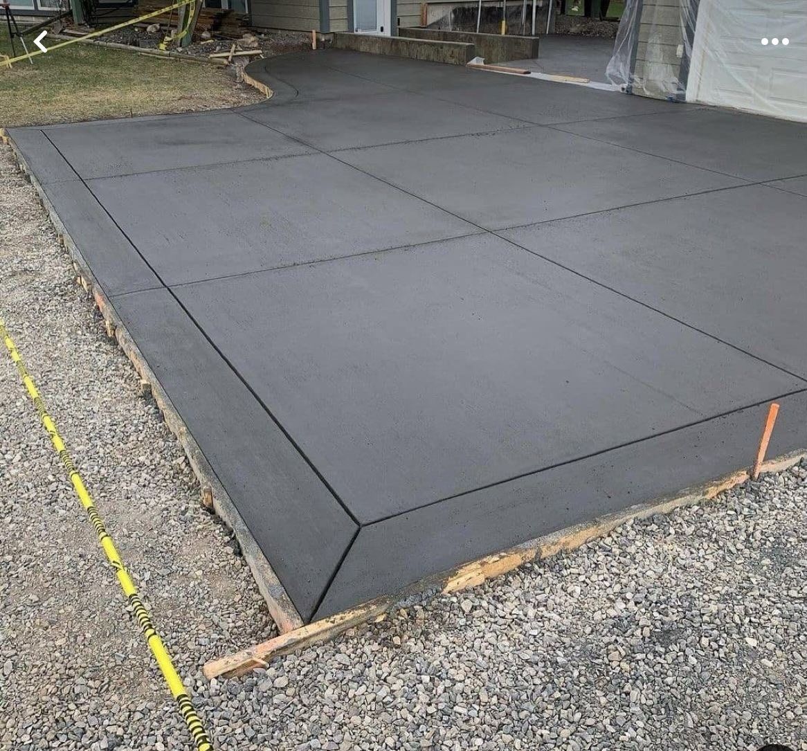 Freshly poured gray concrete driveway slabs beside gravel and a garage entrance
