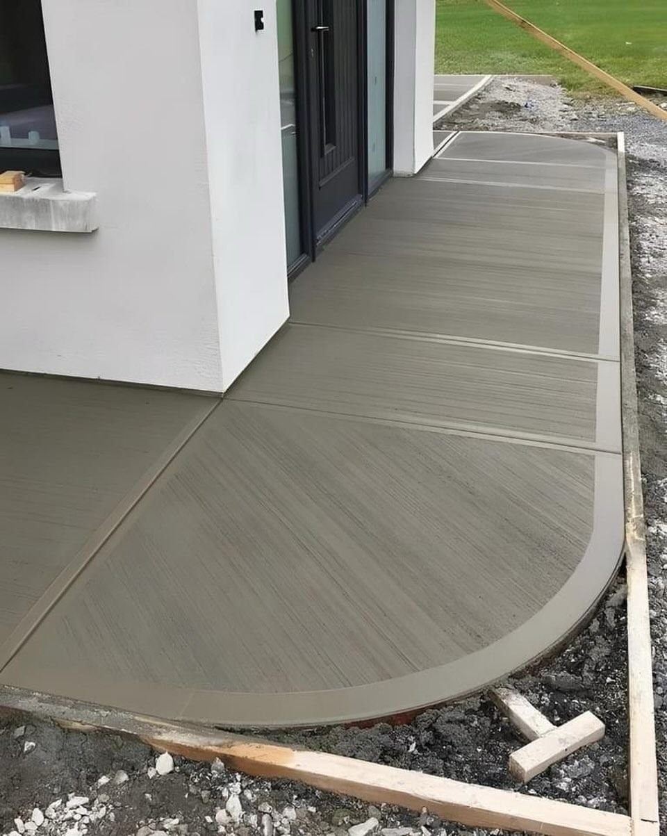 Curved gray concrete patio beside a white house, with a black-framed sliding door and gravel edge