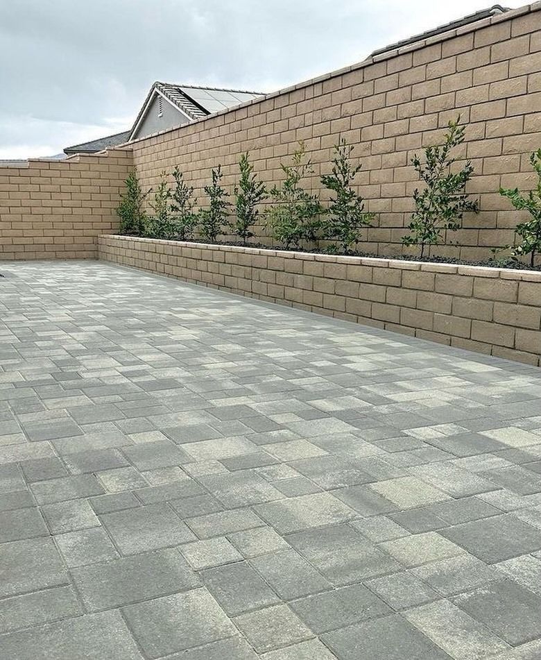 Paved patio with tan block walls and small shrubs along the edge