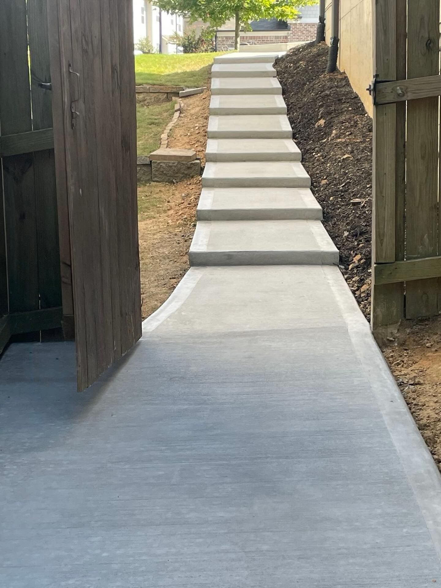 Concrete accessibility ramp leading up a set of steps between wooden fences outdoors
