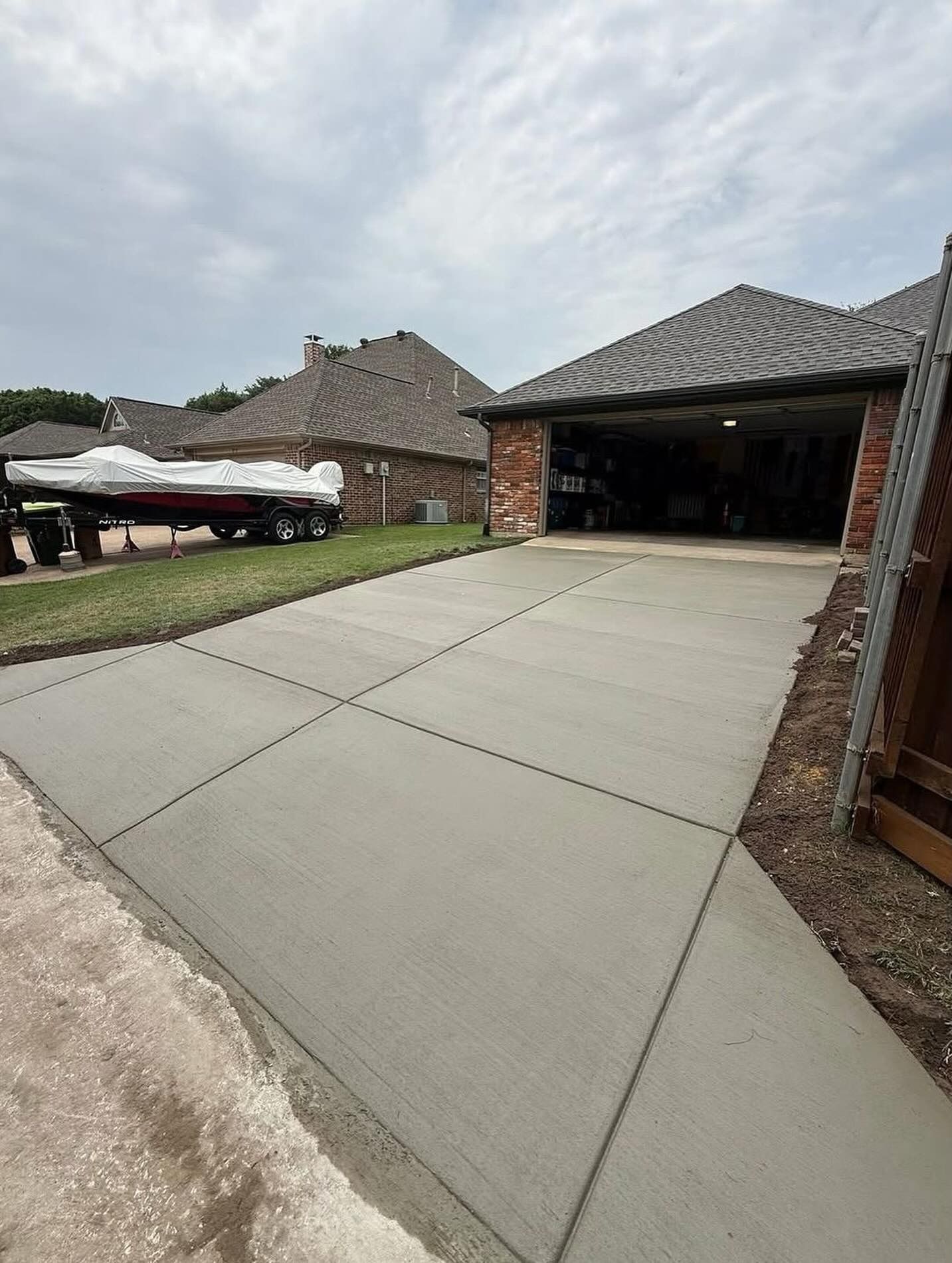 Concrete driveway leading to a brick garage in a suburban neighborhood under cloudy skies