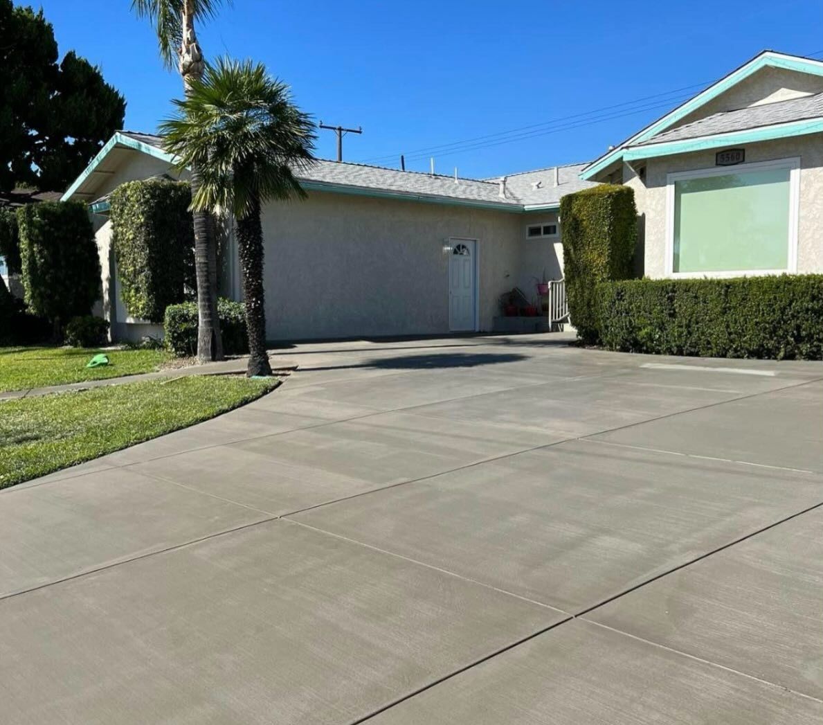 Suburban house with a two-car garage, palm trees, and a wide concrete driveway in bright sunlight
