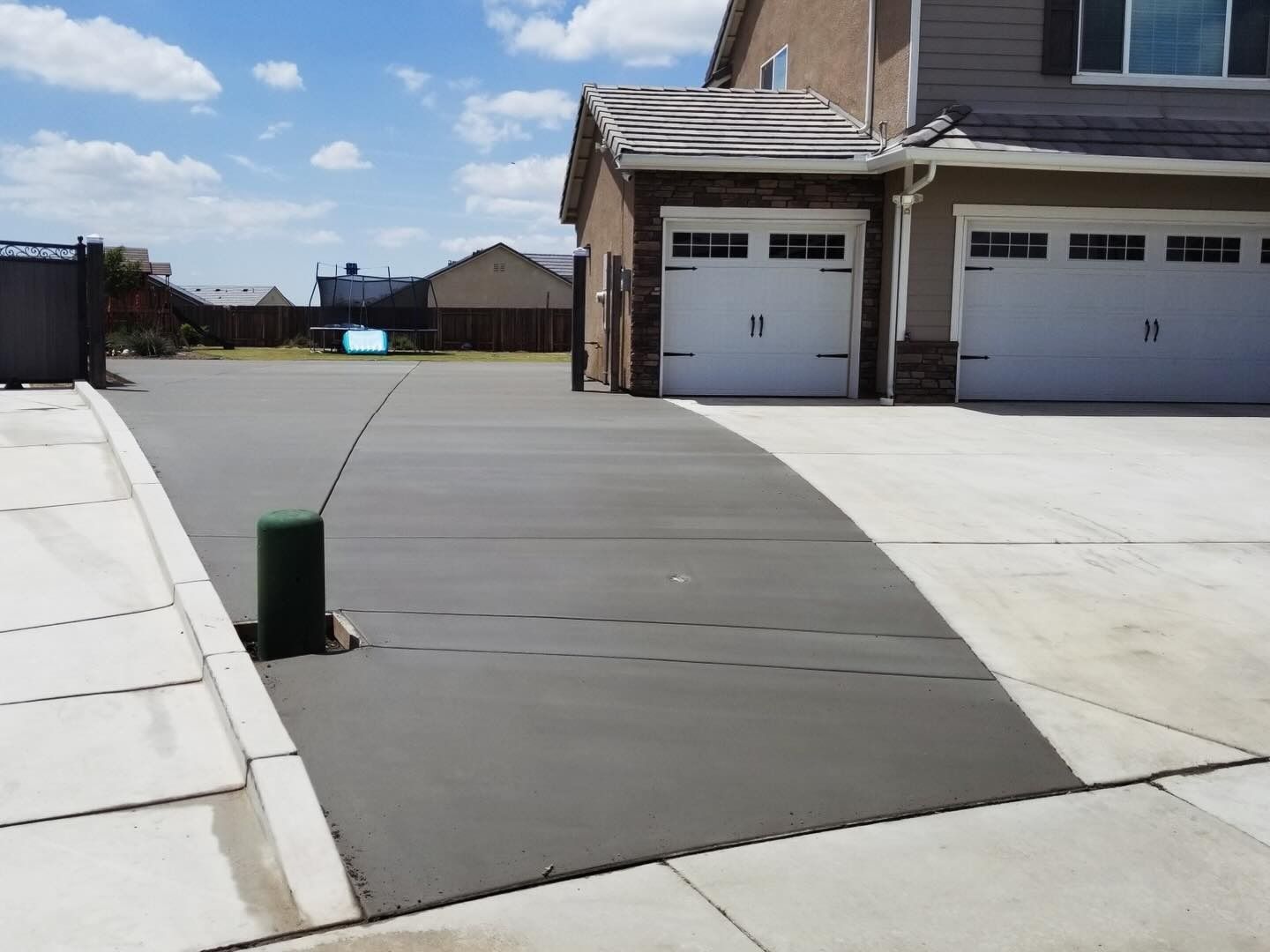 Residential driveway and sidewalk with two garage doors and a green post under clear sky.