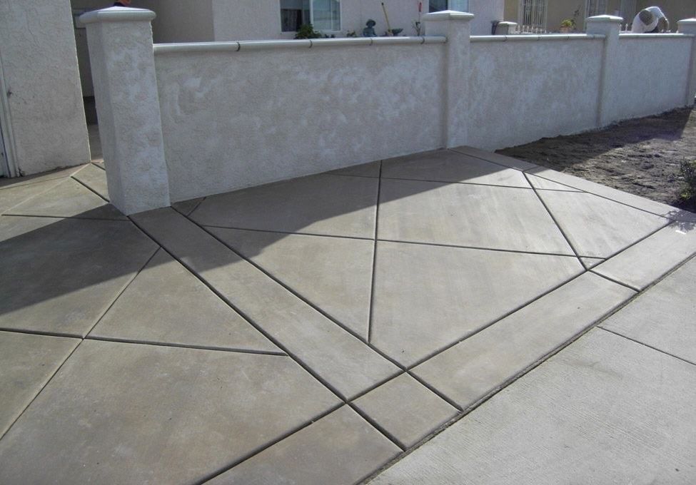 Concrete sidewalk with geometric expansion joints beside a white stucco wall and gate posts.
