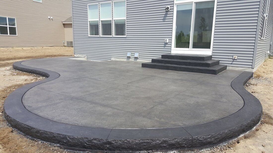 Curved concrete patio beside a gray house with sliding glass doors and black steps