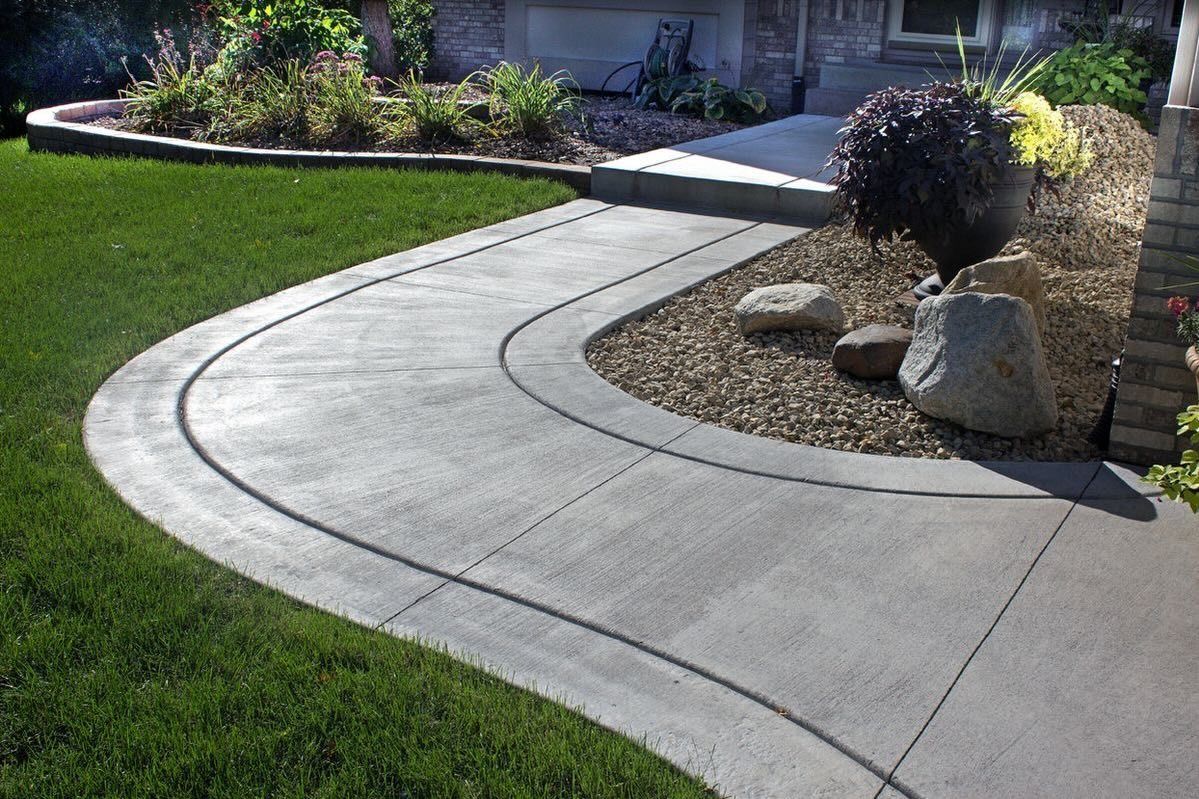 Curved concrete sidewalk through a green lawn beside a rock garden and house path