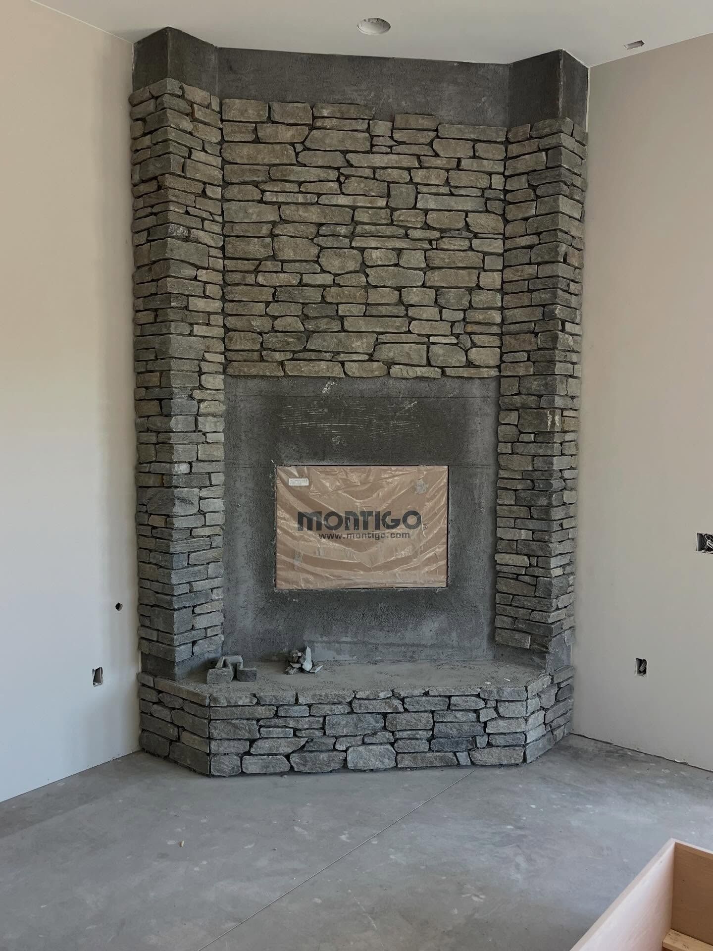 Stone fireplace with a recessed opening in a bare room, centered on a gray wall.