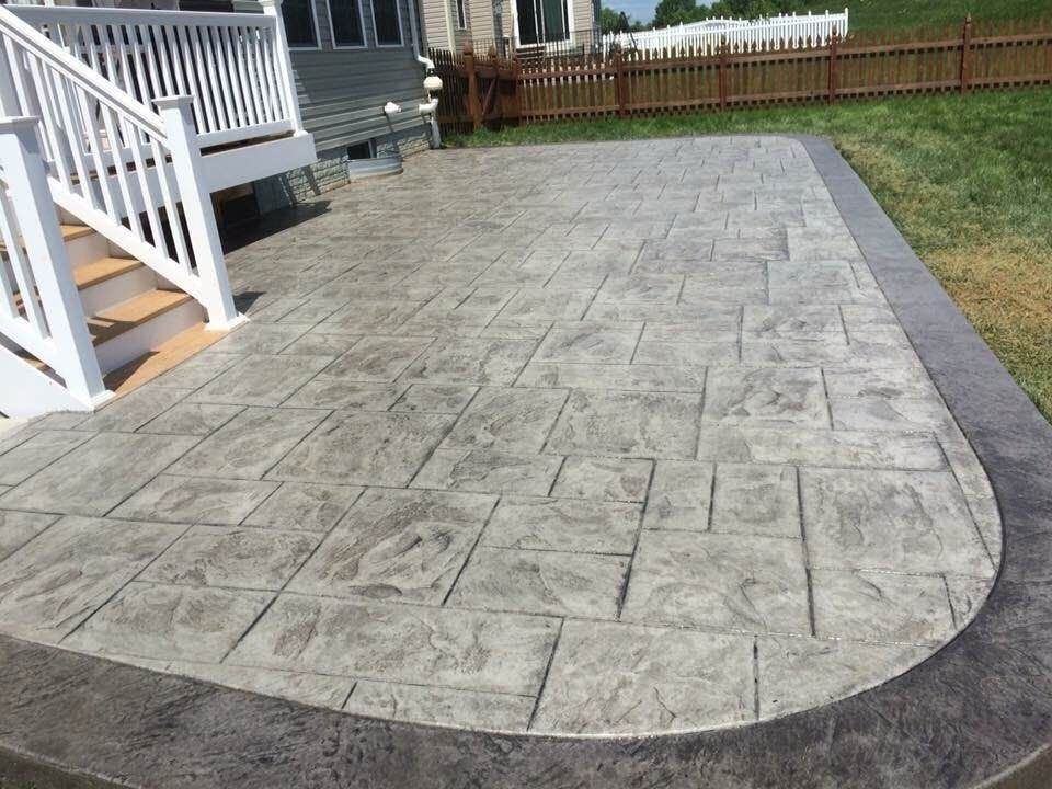 Stamped concrete patio with curved edge beside a white house and wooden fence