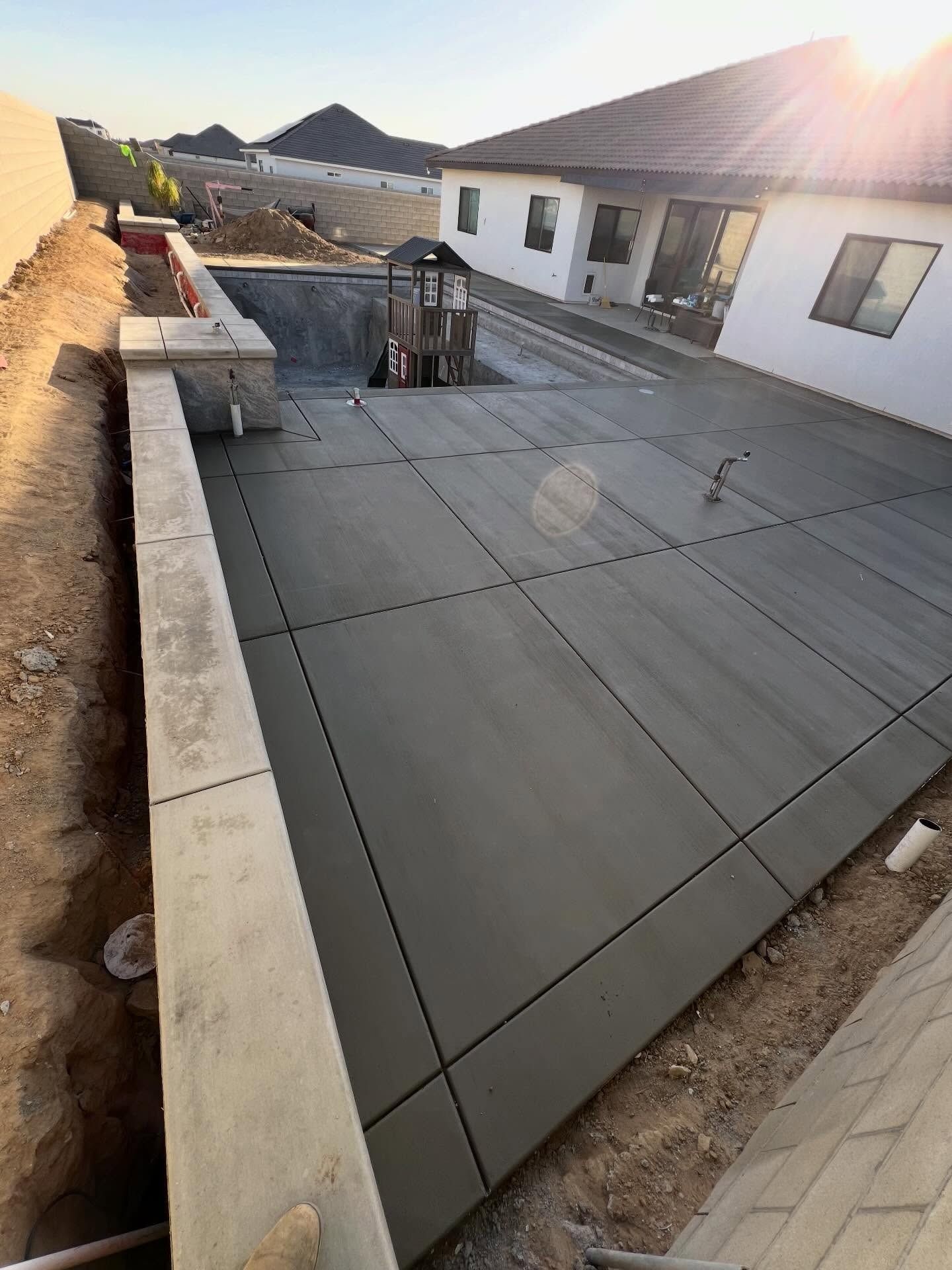 Backyard patio under construction with large gray concrete slab, low walls, and a white house in the background