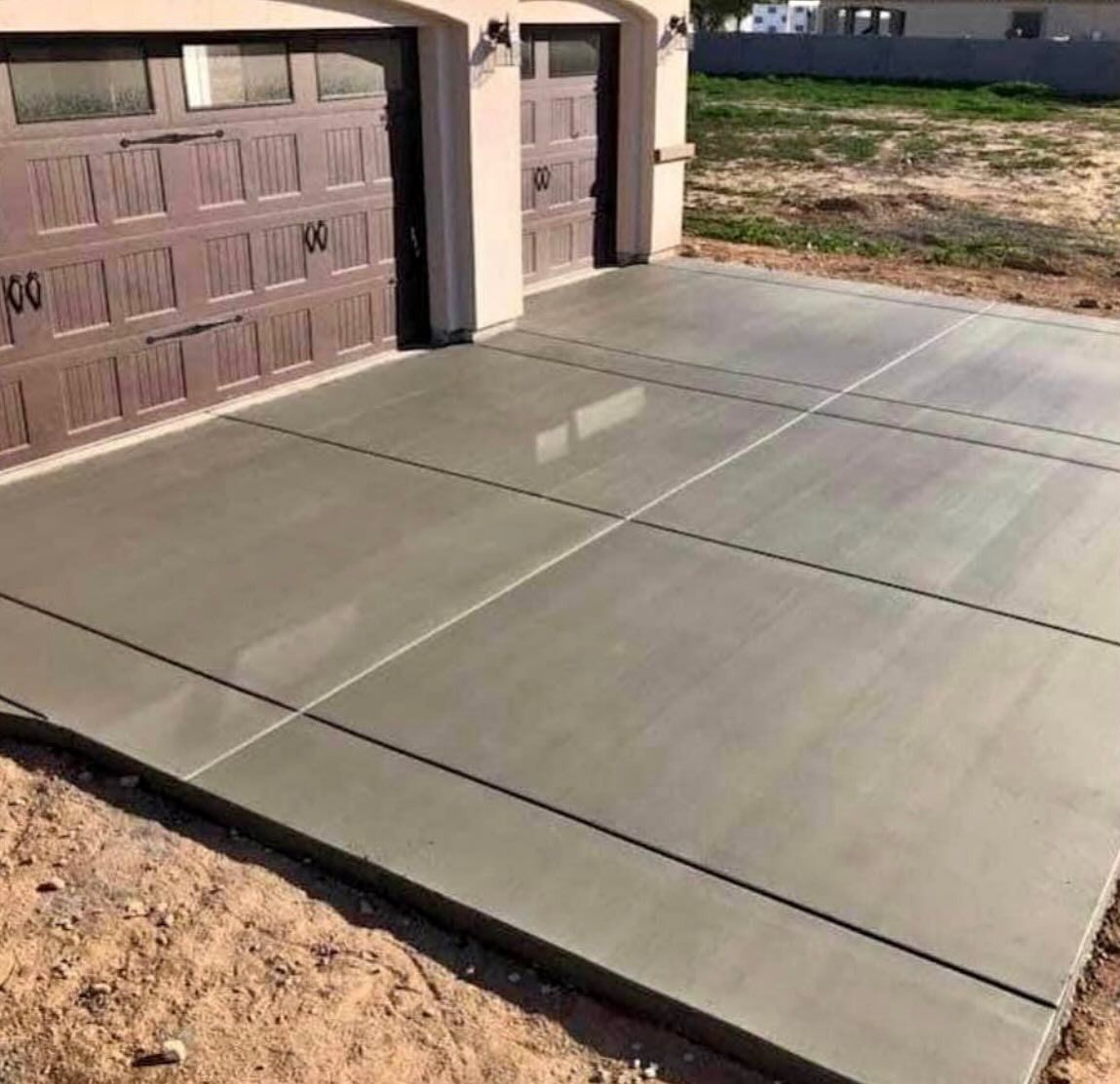 New concrete driveway leading to a garage with tan doors beside a dirt yard