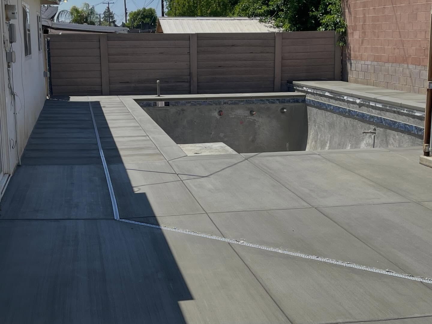 Empty backyard with a concrete pool under construction and wooden fence in the background
