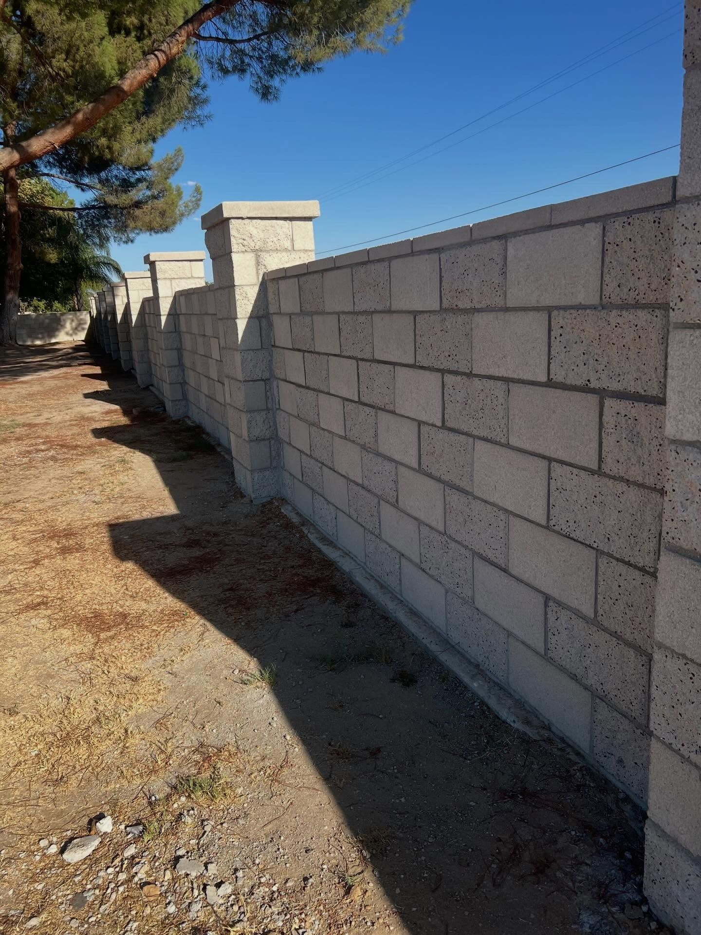 Tall stone block wall along a dirt path beside trees and blue sky