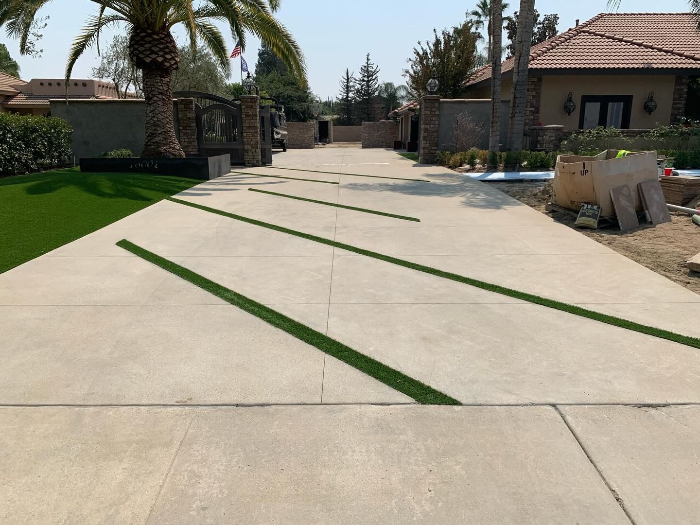 Residential driveway with concrete pavers and green grass strips, leading to a gated house entrance.