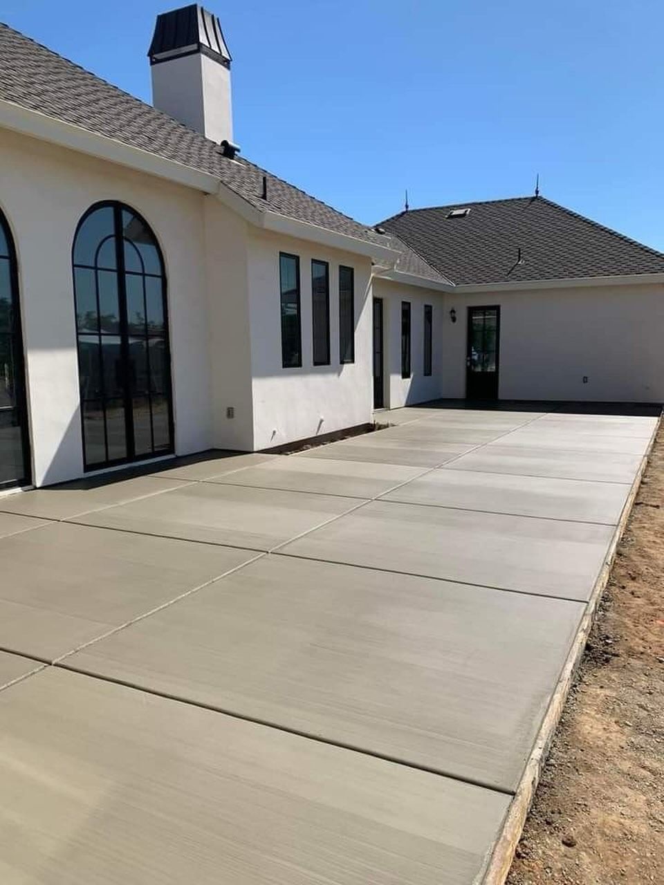 Modern white house with arched windows and a large concrete driveway under a clear blue sky