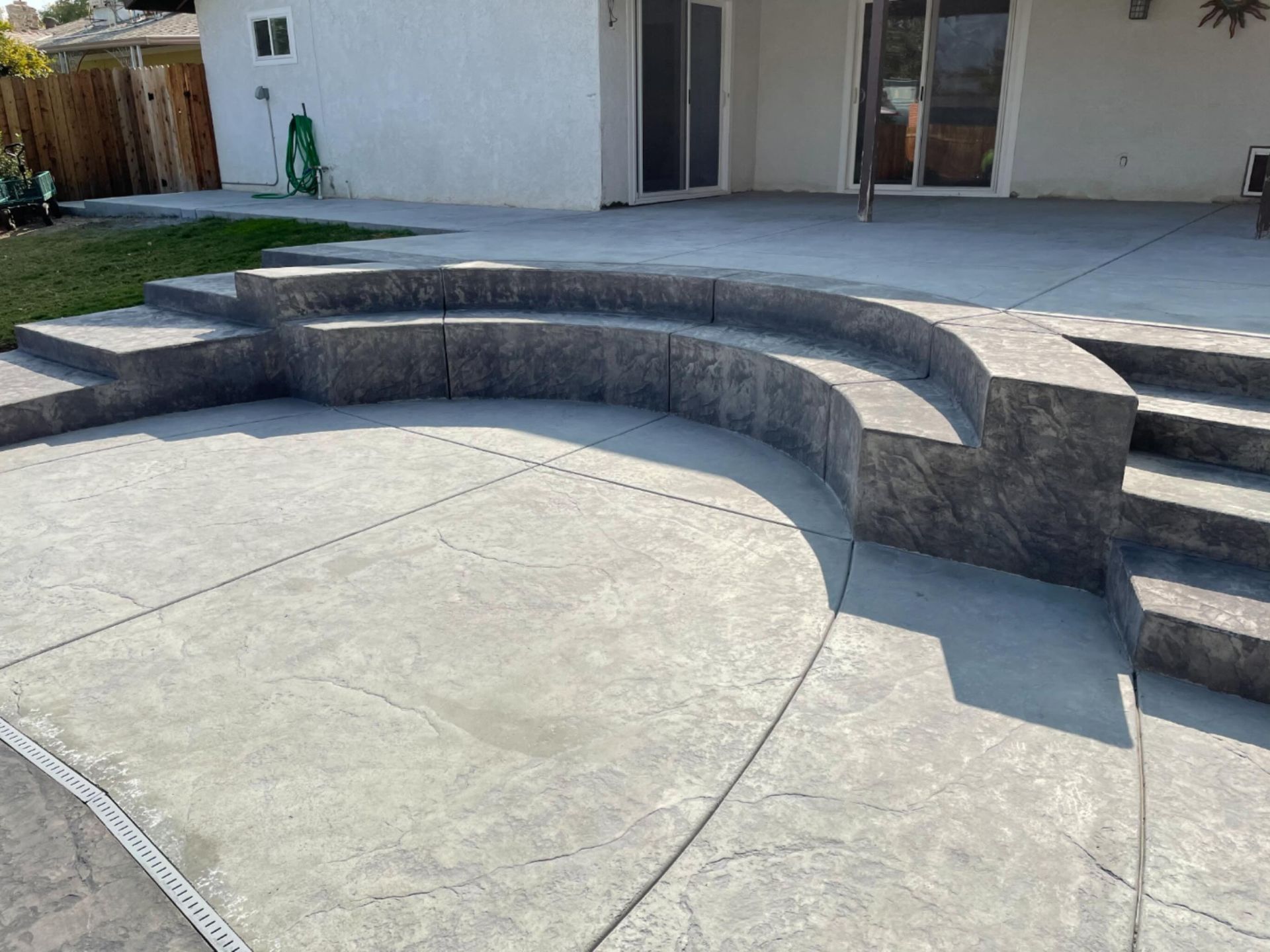 Curved stone seating beside a concrete patio in a backyard courtyard