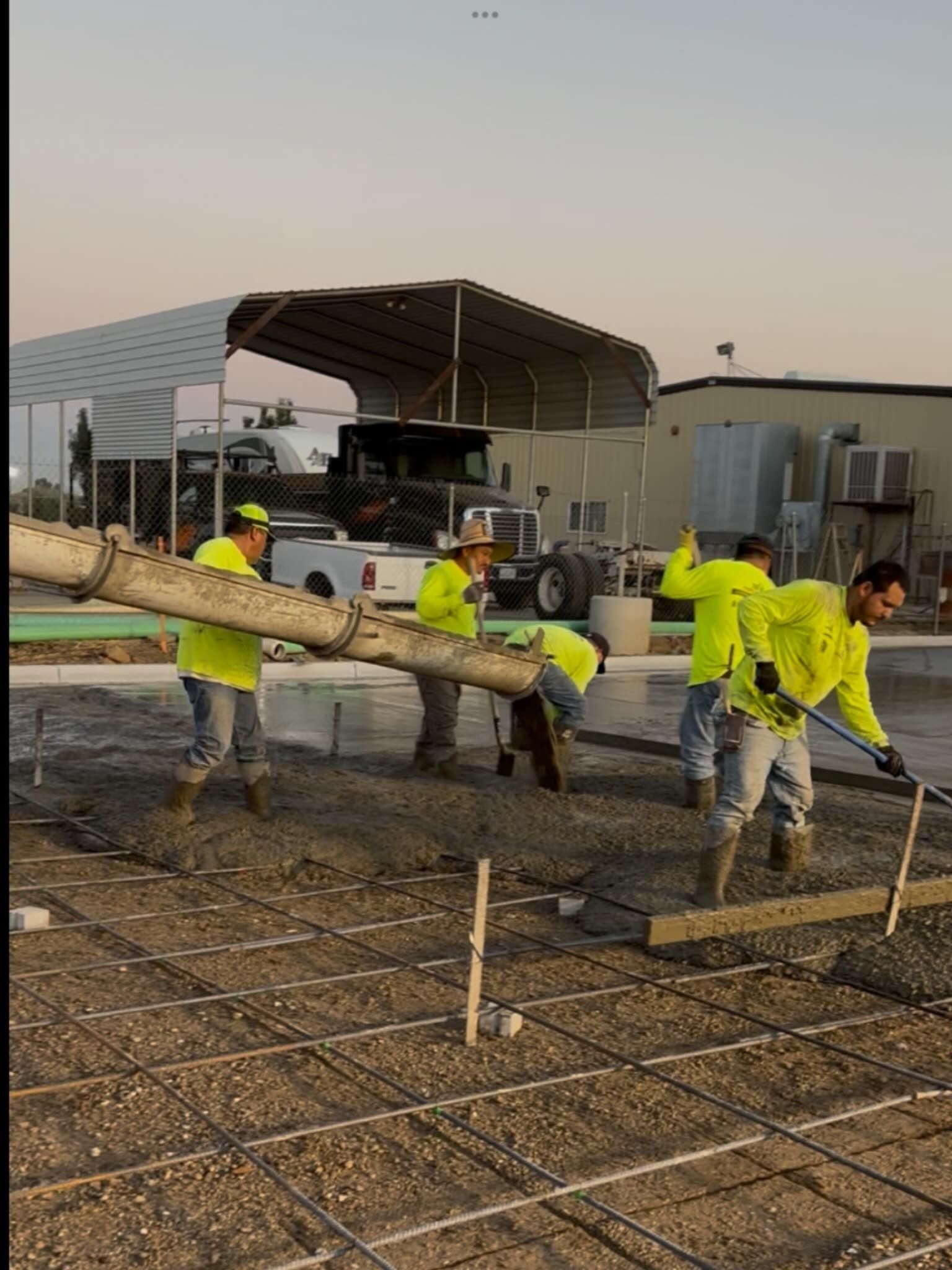 Workers in neon yellow gear leveling concrete with a long tool at a construction site.