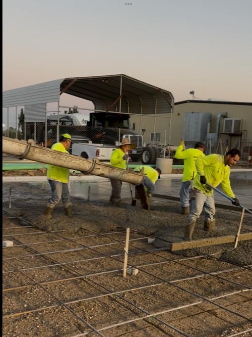 Workers in neon yellow gear leveling concrete with a long tool at a construction site.