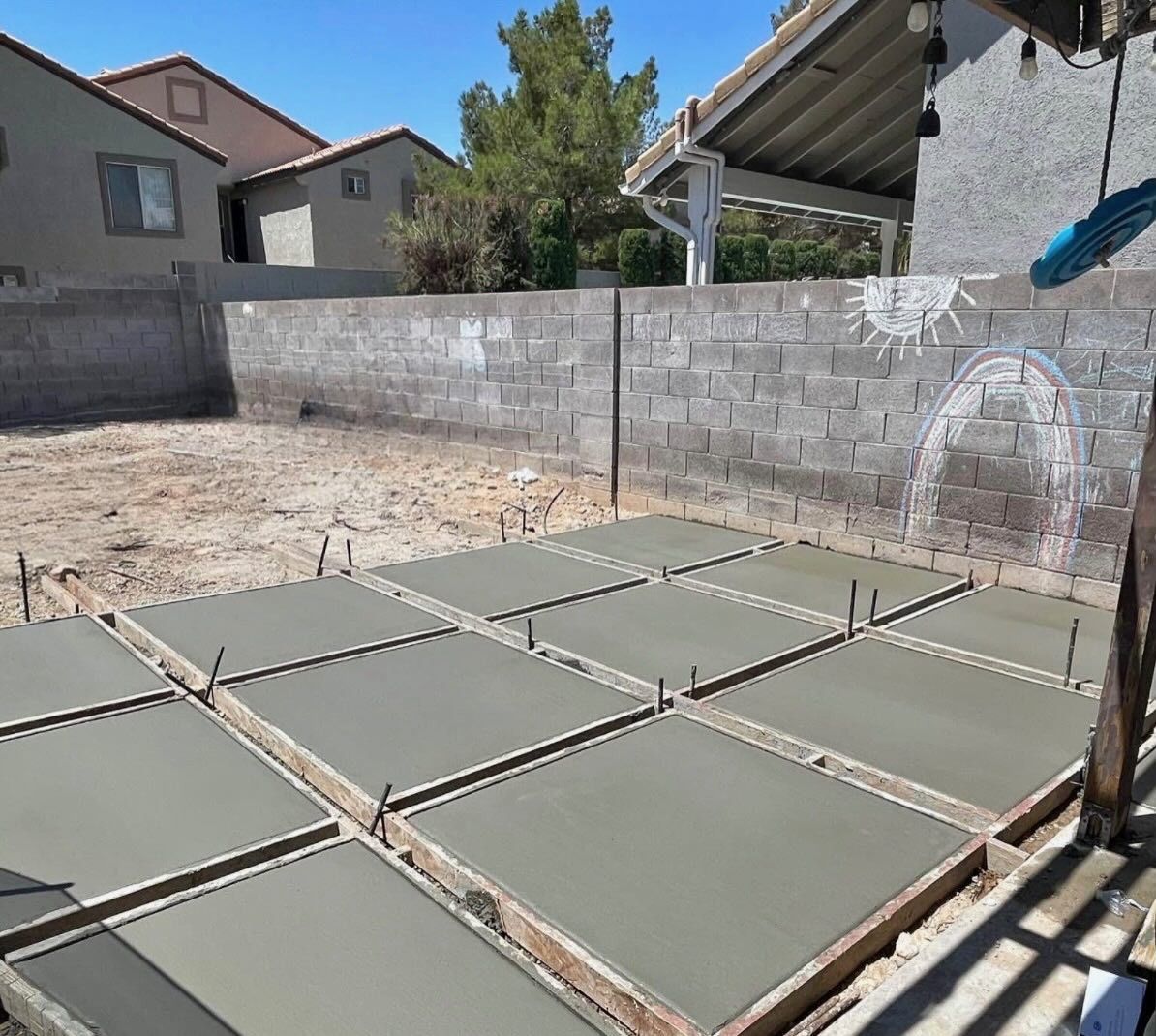 Fresh concrete slabs being poured in a backyard construction area, with block walls and a covered patio.