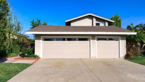 Suburban house with a three-car garage, concrete driveway, and trees in front
