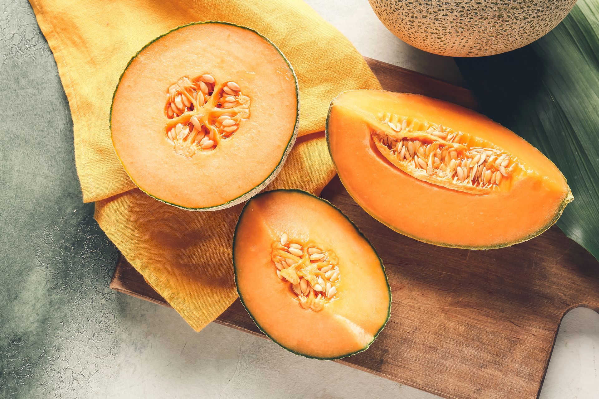 Il melone cantalupo, tagliato a metà, è appoggiato su una tavola di legno con un panno giallo.