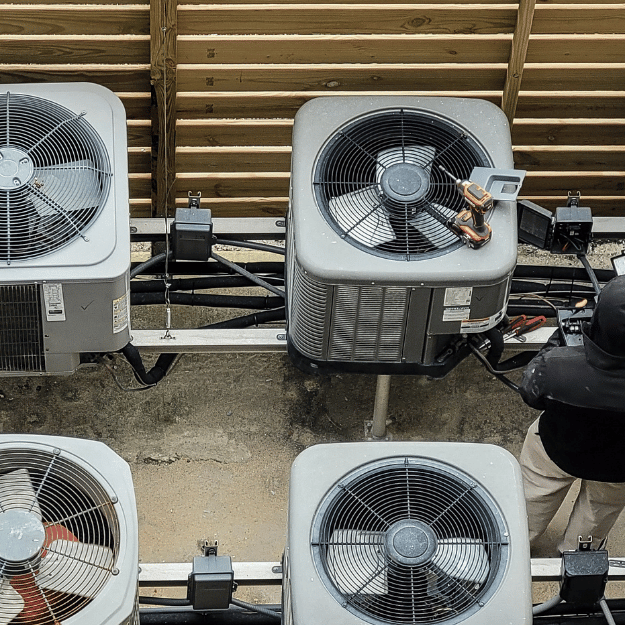 AC units mounted on a wall with a person working on one.