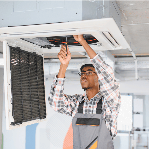 Man in work overalls fixing ceiling air conditioner with a screwdriver.