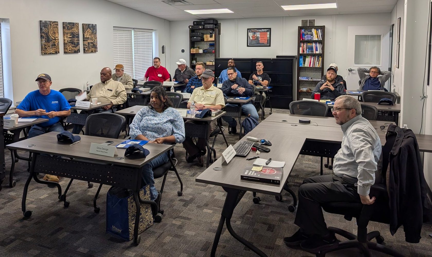 People in office raise hands, lit by overhead lights and computer screens.