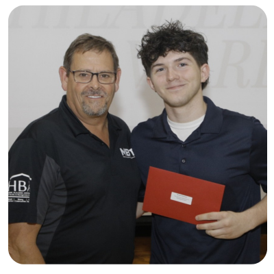 A young man smiles, holding documents and a bag, flanked by two people, likely at an awards ceremony.