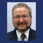 Man with glasses and beard, smiling in suit and tie.