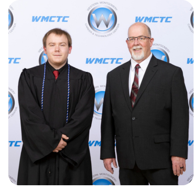 Student in graduation gown receives an award from a man in a suit. Stage with blue curtains in background.