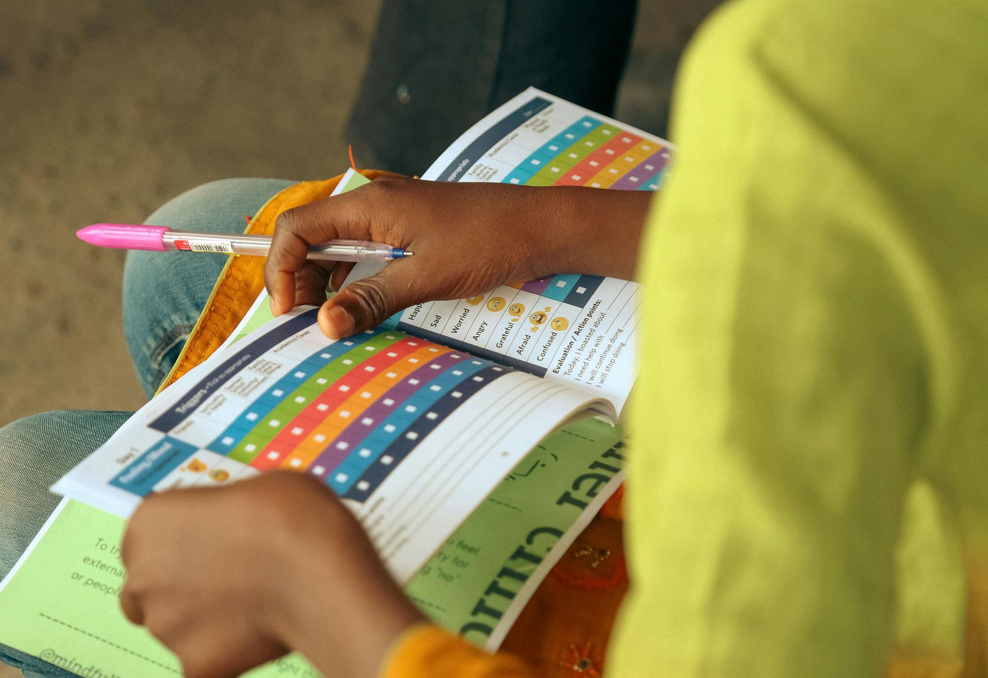Person holding open workbook with colorful stickers, sitting, indoors.