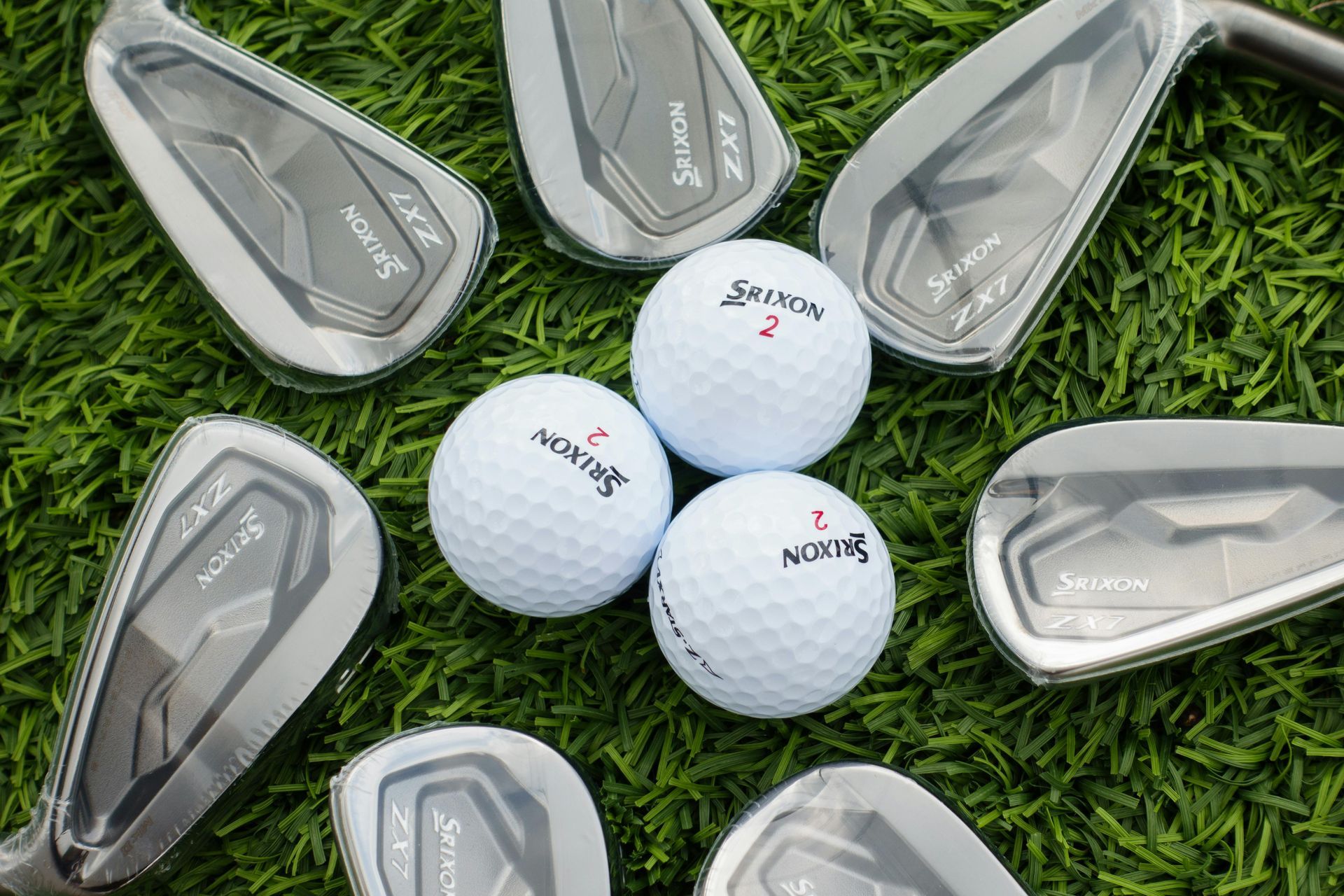 Golf clubs and golf balls arranged on green grass.
