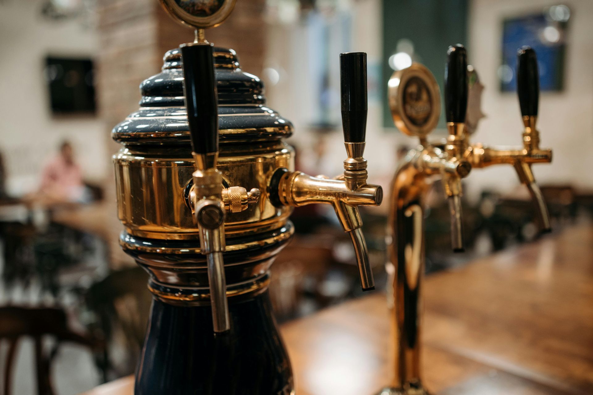 Close-up of ornate gold and dark blue beer taps on a bar, with a blurry interior background.