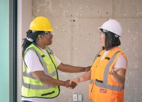 Two construction workers in hard hats and safety vests talking on a renovation site