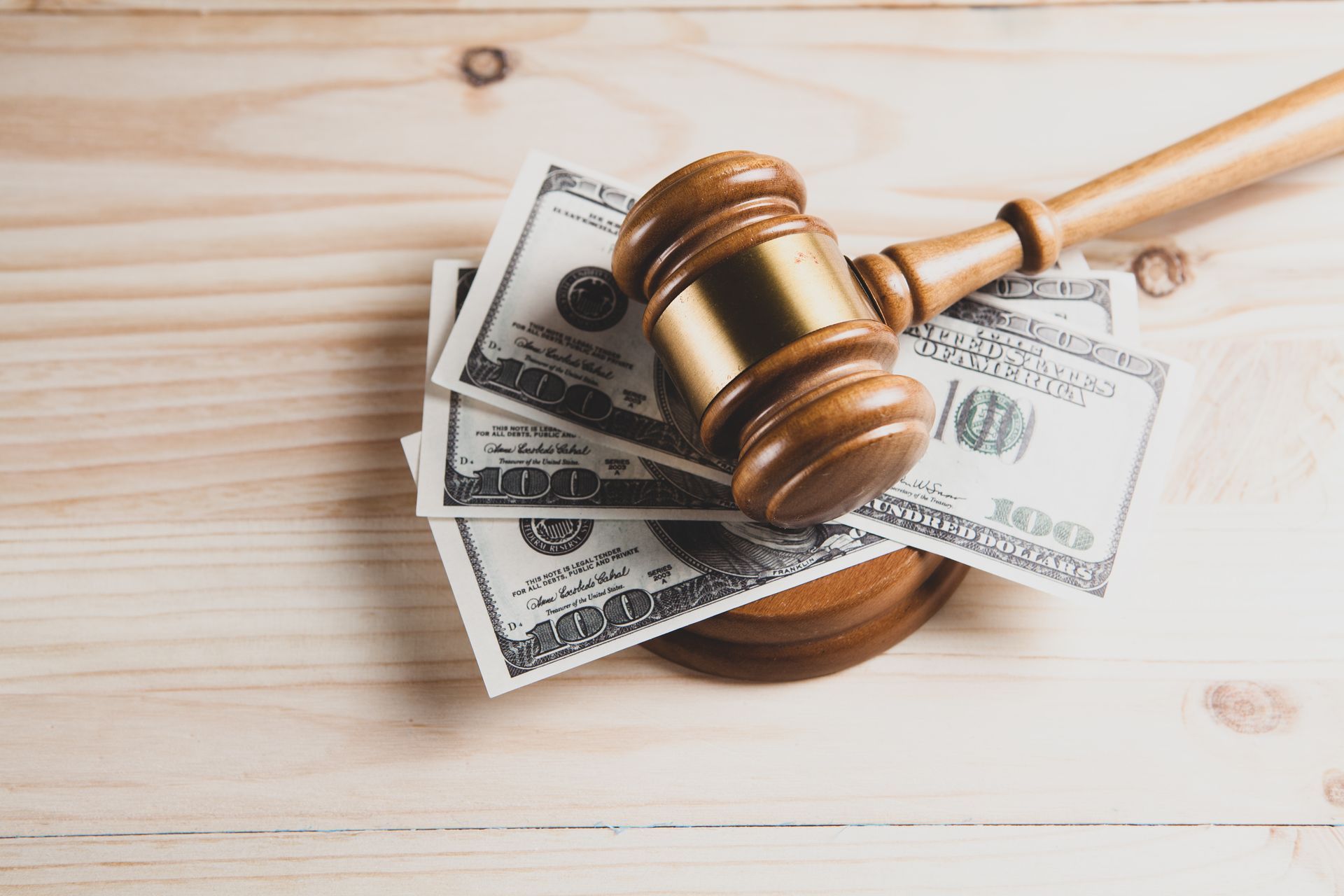 A wooden judge 's gavel sitting on top of a pile of money on a wooden table.