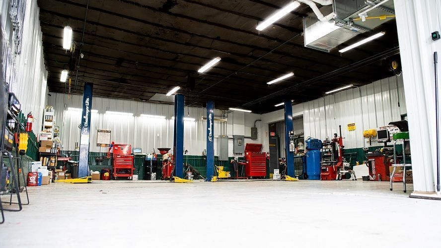 Wide auto repair shop interior with cars, tool cabinets, lifts, and bright overhead lights | Advanced Car Care Center LLC