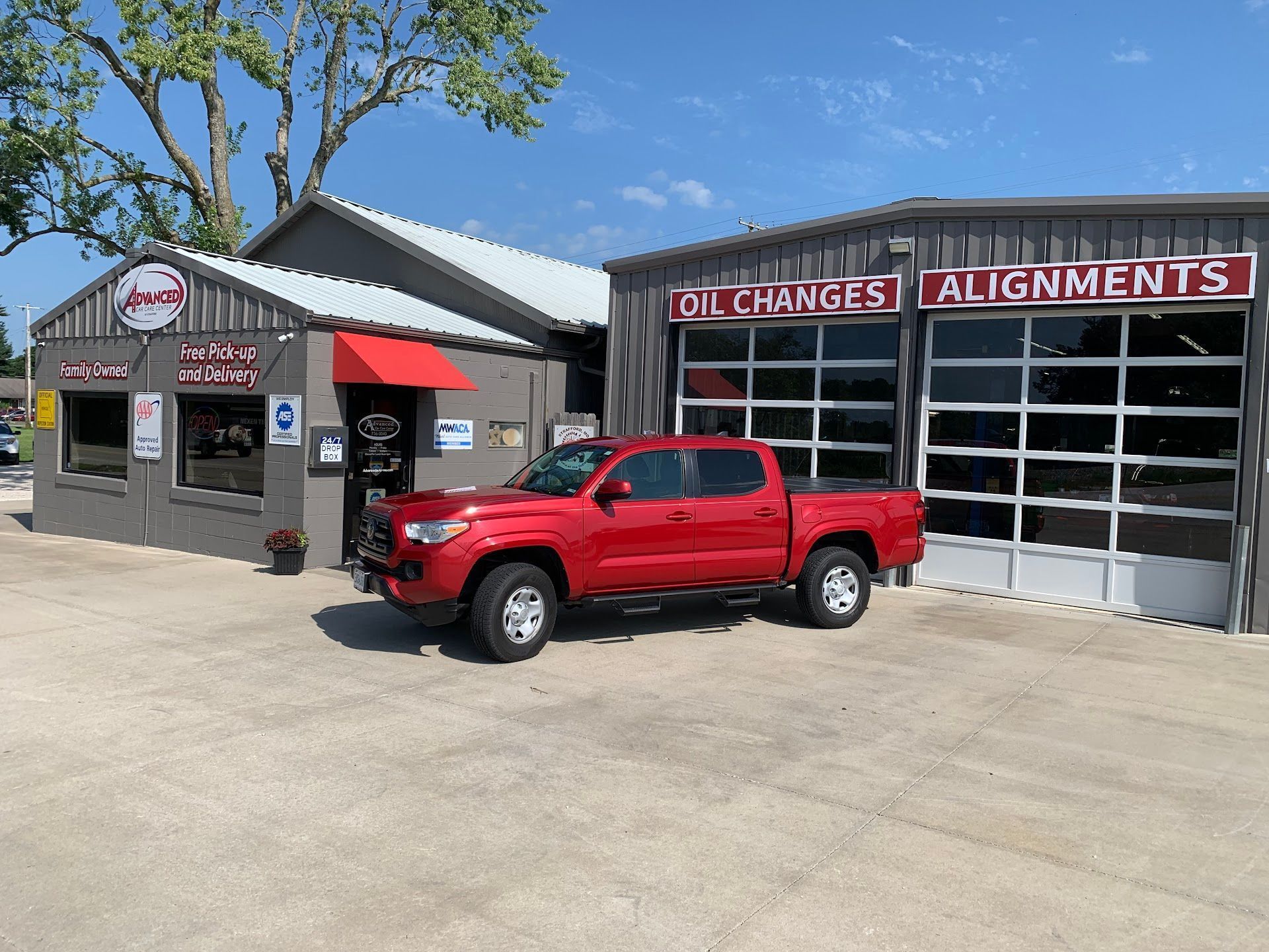 Red pickup truck parked outside a tire and alignment shop with garage bays | Advanced Car Care Center LLC