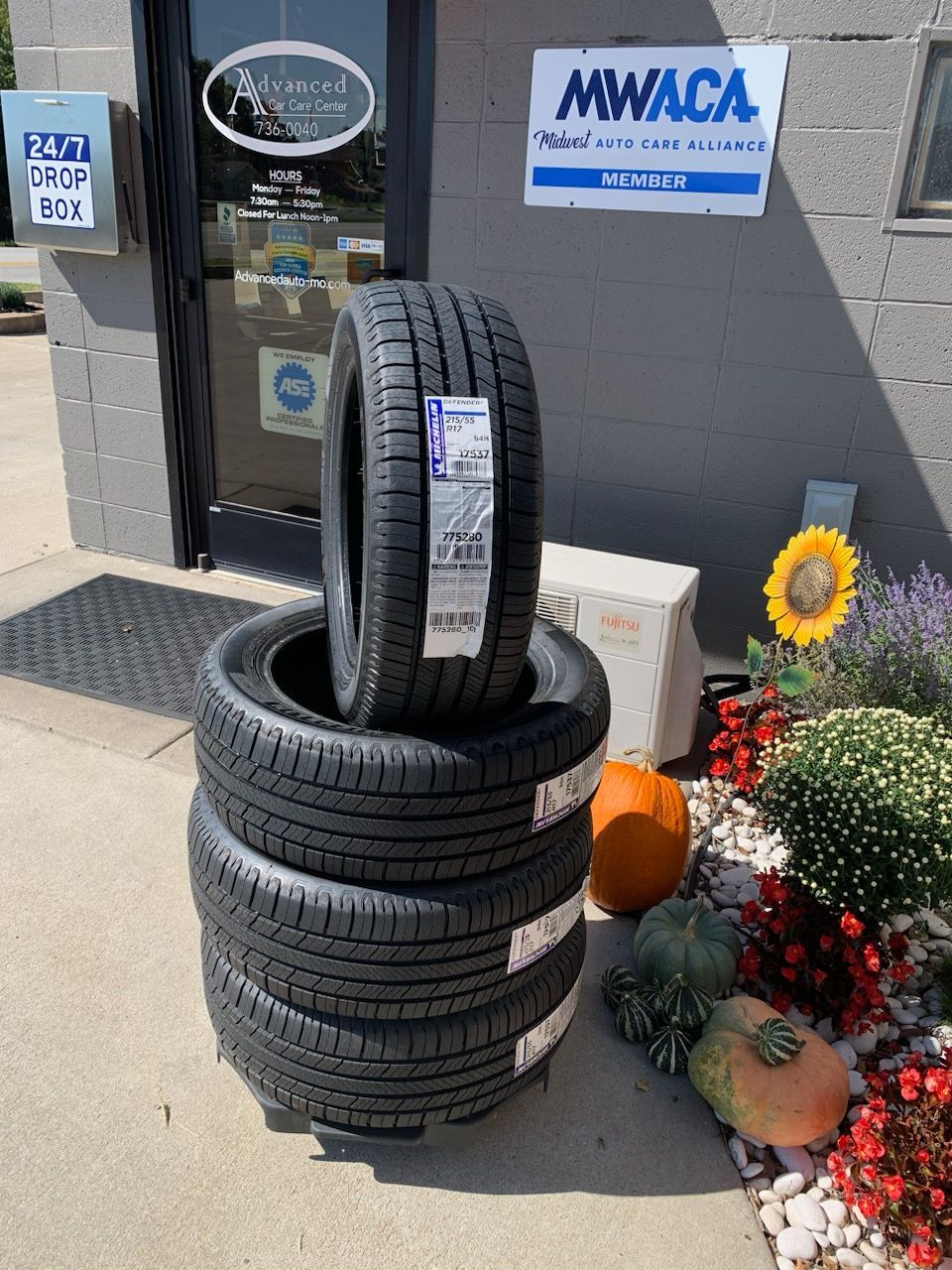 Stacked tires displayed outside a store beside a pumpkin and fall flowers. | Advanced Car Care Center LLC