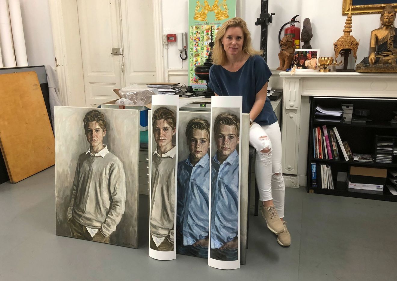 Vrouw zit in een kunststudio naast grote portretschilderijen op opgerolde doeken.